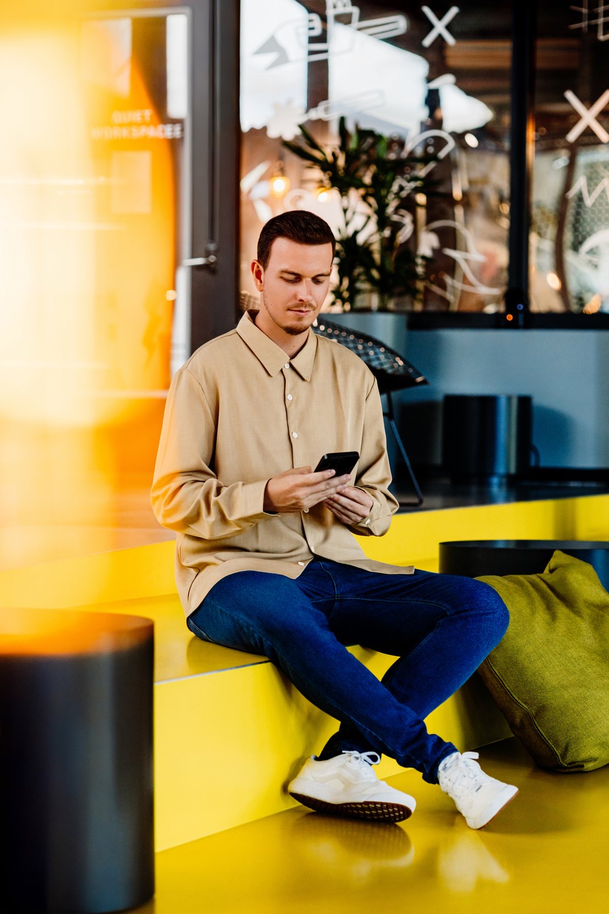 Willem Kooiman op de gele bank met zijn telefoon